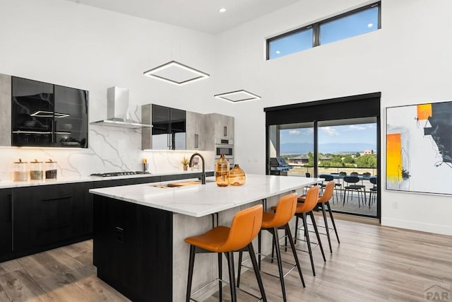 kitchen with dark cabinetry, stainless steel appliances, a sink, wall chimney range hood, and modern cabinets