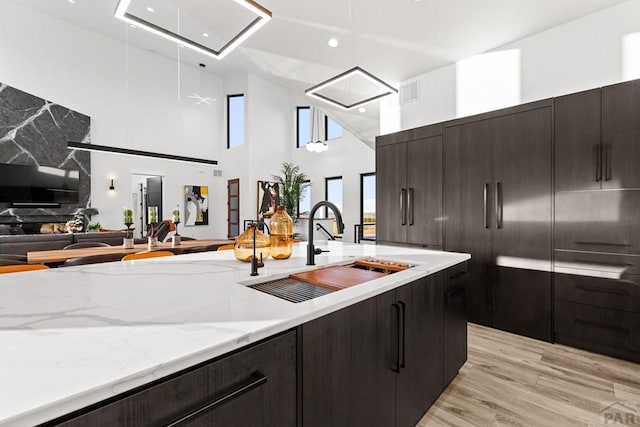 kitchen with light stone counters, visible vents, a sink, open floor plan, and light wood-type flooring