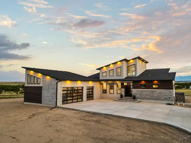 contemporary home with a garage, stone siding, driveway, and stucco siding