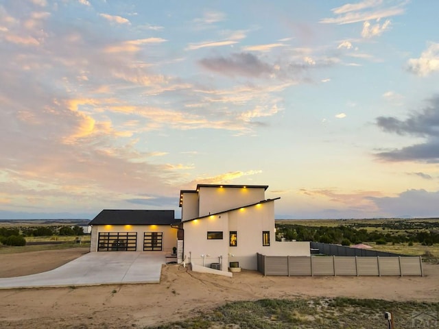 property exterior at dusk featuring a detached garage, fence, and stucco siding