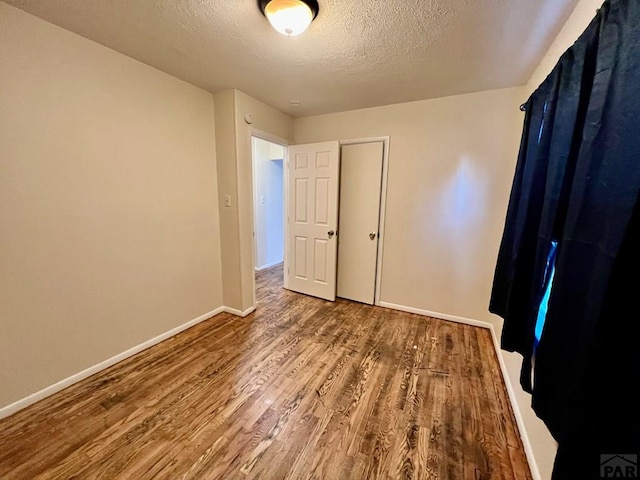 unfurnished bedroom featuring baseboards, a textured ceiling, and wood finished floors