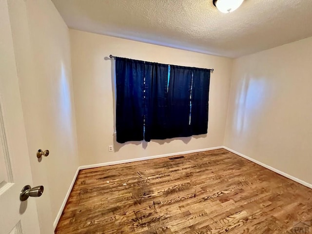 empty room featuring visible vents, a textured ceiling, baseboards, and wood finished floors