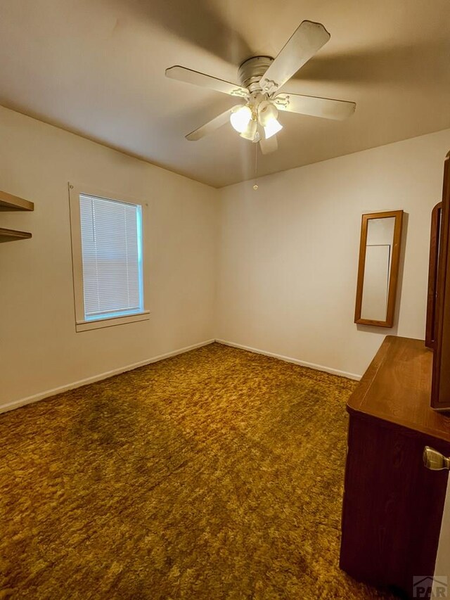 empty room featuring dark carpet, a ceiling fan, and baseboards