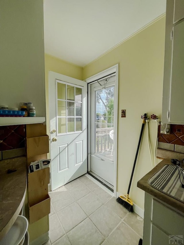 doorway with light tile patterned floors, ornamental molding, and baseboards