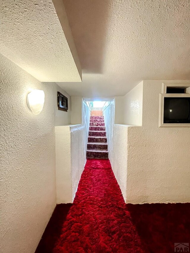 corridor featuring stairway, carpet floors, a textured wall, and a textured ceiling