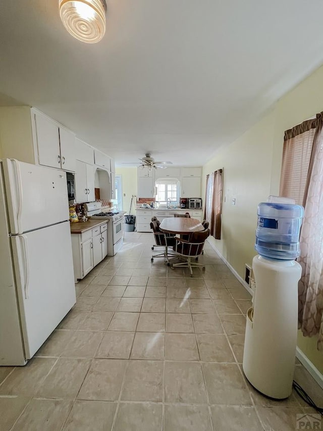 kitchen featuring white appliances, baseboards, white cabinets, ceiling fan, and light tile patterned flooring