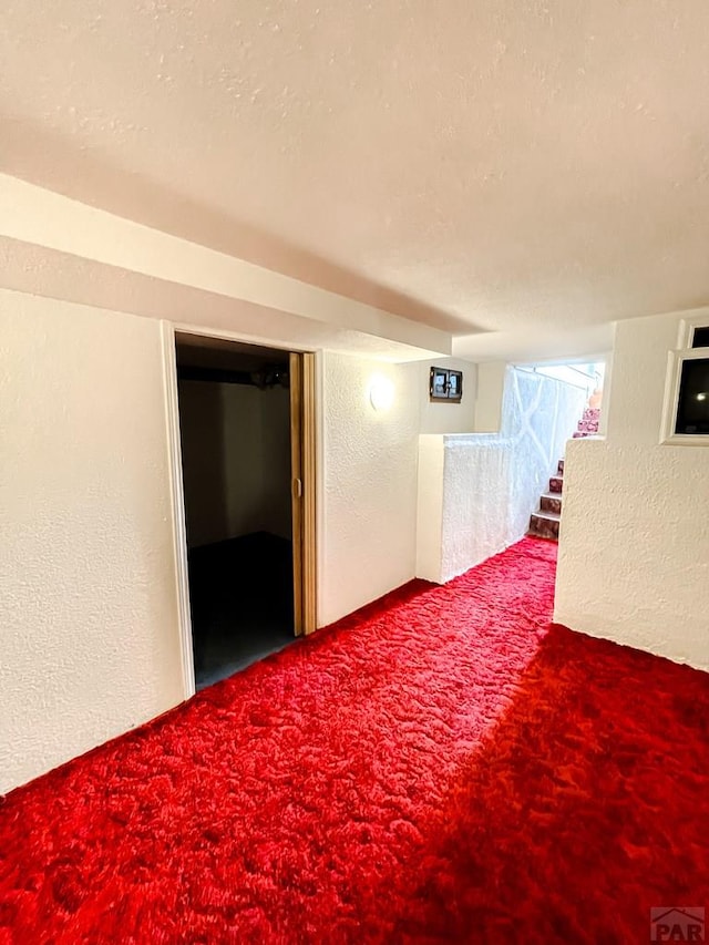 below grade area with carpet, a textured wall, a textured ceiling, and stairs