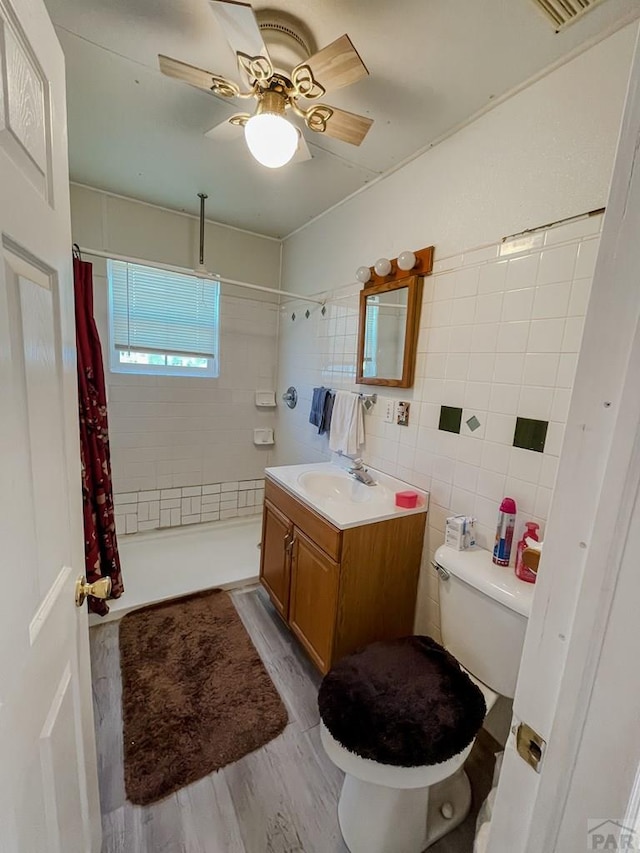 bathroom featuring toilet, tiled shower, wood finished floors, and tile walls