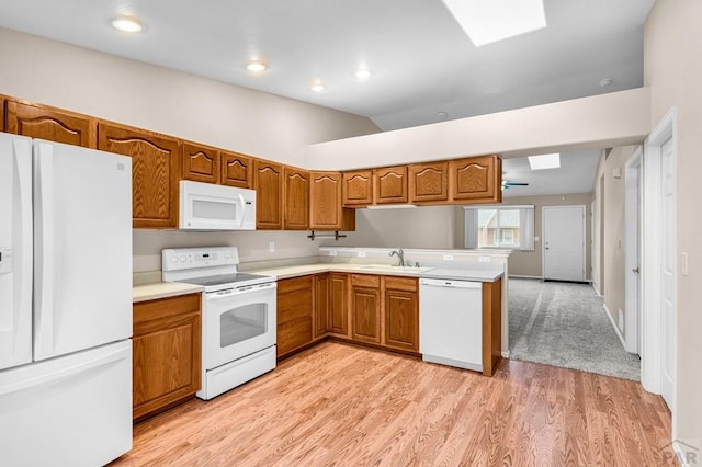 kitchen with a sink, white appliances, brown cabinets, light wood-style flooring, and light countertops