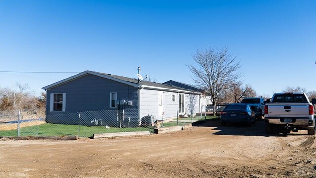 view of side of home with dirt driveway, a yard, and fence