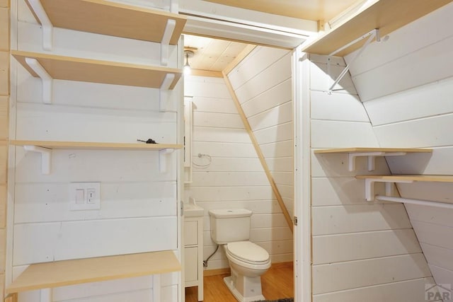 bathroom featuring toilet, wood walls, and wood finished floors