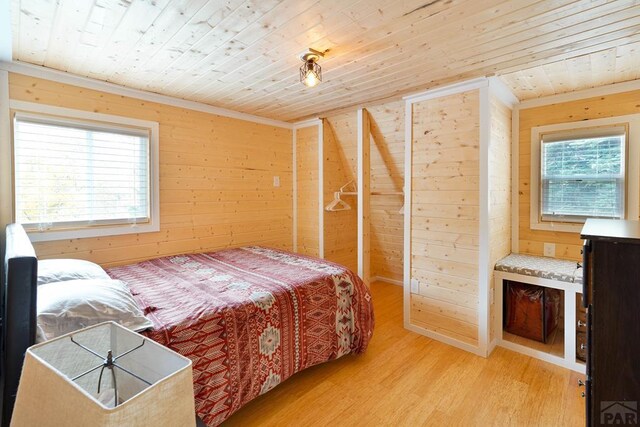 bedroom featuring ornamental molding, wooden ceiling, wood walls, and light wood finished floors