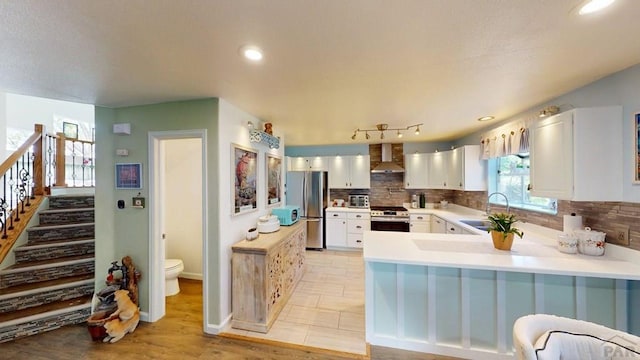 356 S Littler Dr, Pueblo West, CO 81007 - kitchen featuring a sink, stainless steel appliances, wall chimney exhaust hood, a peninsula, and tasteful backsplash