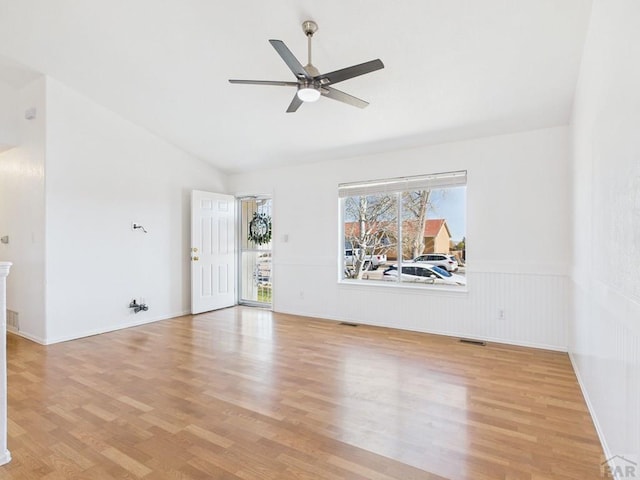 unfurnished living room featuring wainscoting, light wood-style flooring, a ceiling fan, and vaulted ceiling