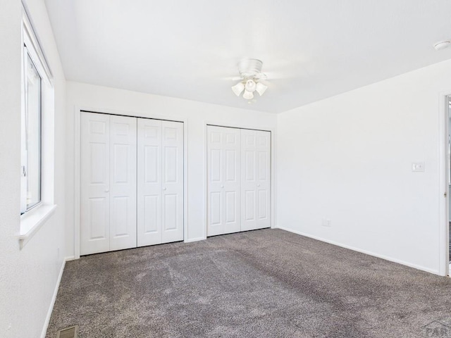 unfurnished bedroom featuring visible vents, baseboards, multiple closets, carpet floors, and a ceiling fan