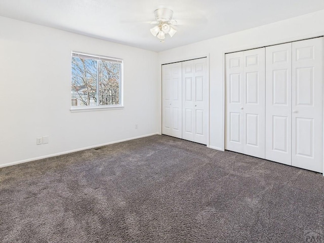 unfurnished bedroom featuring ceiling fan, baseboards, multiple closets, and dark colored carpet