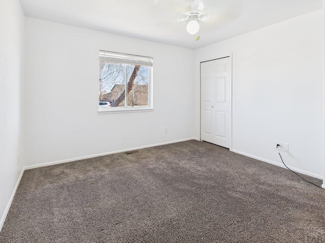 unfurnished bedroom with a ceiling fan, visible vents, baseboards, a closet, and dark carpet