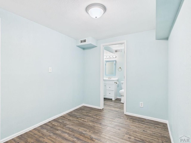 unfurnished bedroom with wood finished floors, visible vents, ensuite bathroom, and baseboards