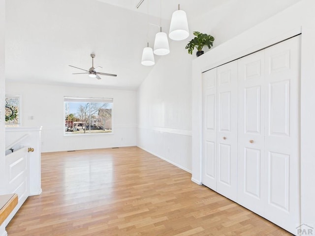 unfurnished living room with light wood-type flooring, lofted ceiling, ceiling fan, and wainscoting