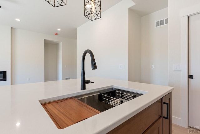 kitchen with light countertops, a sink, visible vents, and pendant lighting