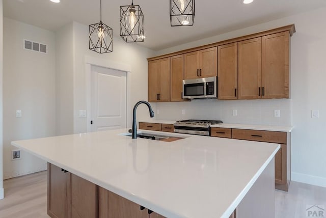 kitchen with a center island with sink, stainless steel appliances, light countertops, and decorative light fixtures