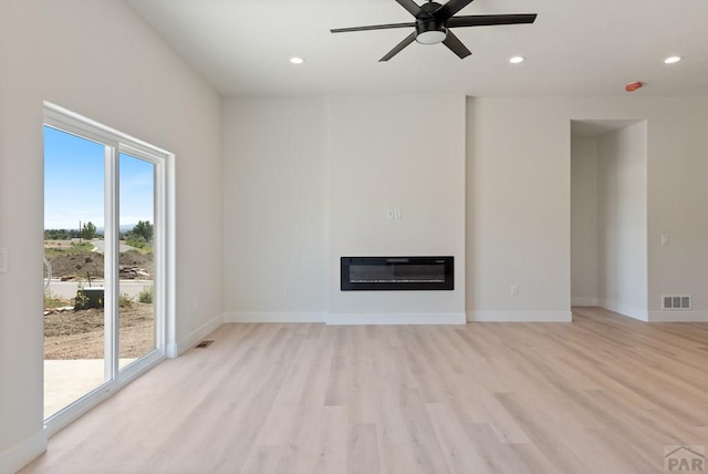 unfurnished living room with visible vents, a glass covered fireplace, heating unit, light wood-style floors, and recessed lighting