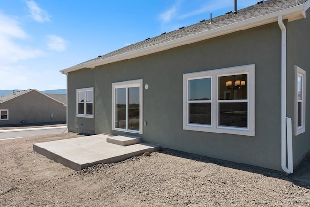 back of property with a shingled roof, a patio area, and stucco siding