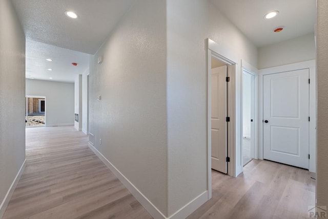 hall with recessed lighting, baseboards, a textured ceiling, and light wood finished floors