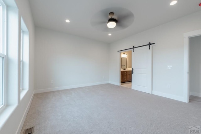 unfurnished bedroom featuring baseboards, a barn door, visible vents, and recessed lighting