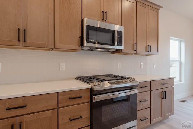 kitchen with baseboards, visible vents, stainless steel appliances, light countertops, and backsplash