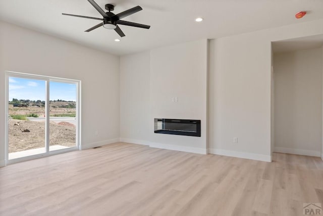 unfurnished living room with recessed lighting, baseboards, light wood-style floors, heating unit, and a glass covered fireplace