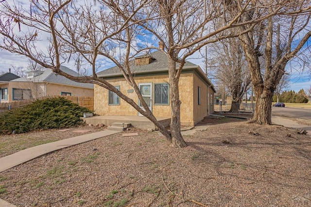 view of side of home featuring roof with shingles, fence, and stucco siding