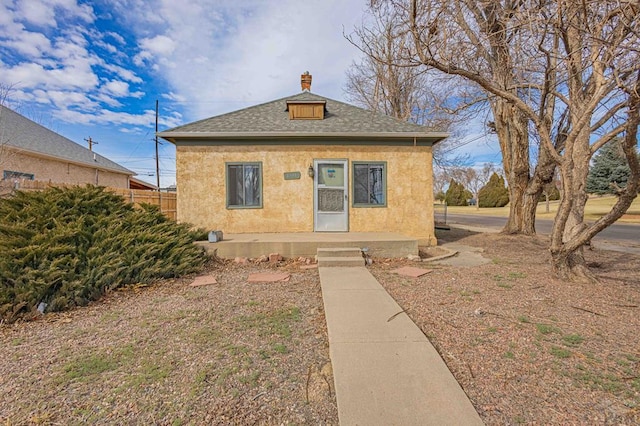 view of front facade with roof with shingles, fence, a chimney, and stucco siding