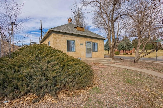 exterior space with stucco siding, a chimney, and roof with shingles