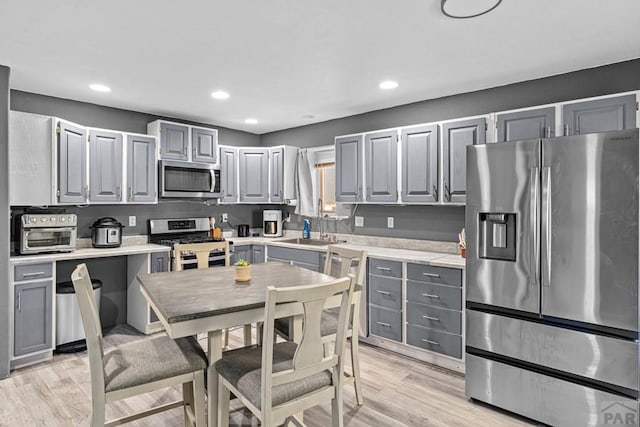 kitchen with appliances with stainless steel finishes, light countertops, light wood-style flooring, and gray cabinetry