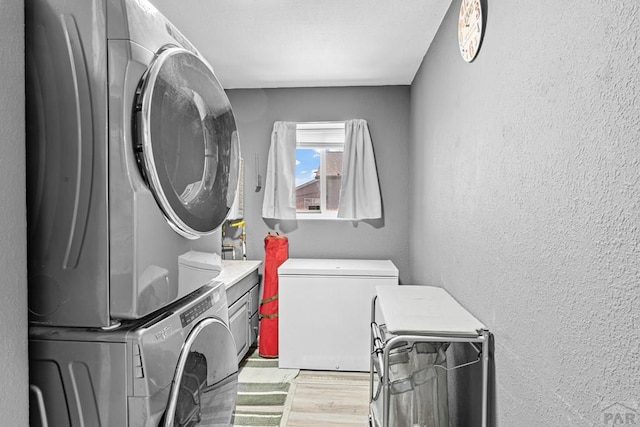 laundry area with stacked washer / drying machine, laundry area, a textured wall, and light wood finished floors