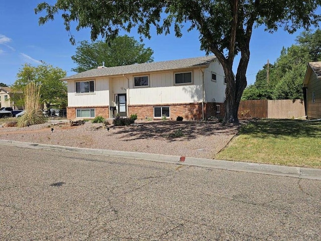 raised ranch with brick siding, a front yard, and fence