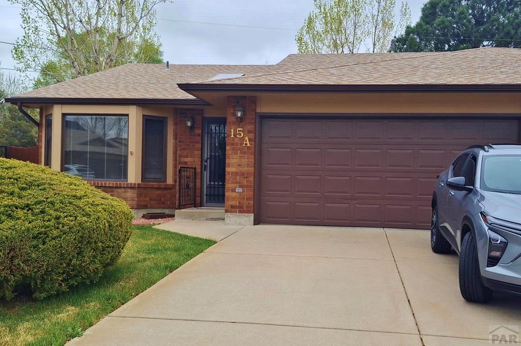 view of front of home with concrete driveway, brick siding, roof with shingles, and a garage
