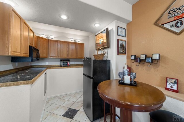 kitchen featuring light tile patterned floors, dark countertops, recessed lighting, freestanding refrigerator, and black microwave