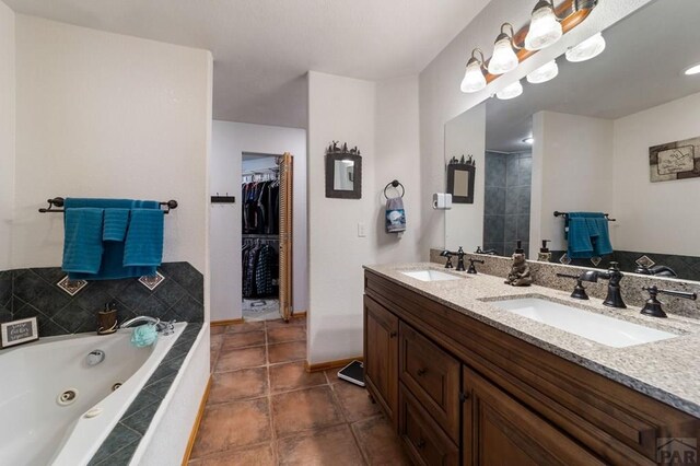 bathroom featuring double vanity, a tub with jets, a spacious closet, and a sink