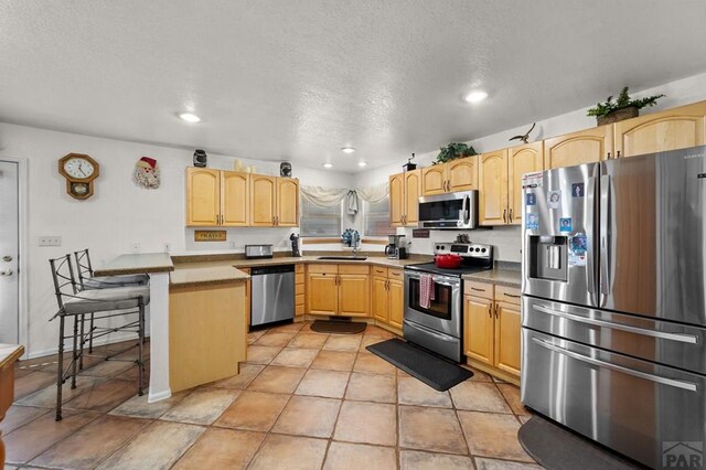 kitchen featuring stainless steel appliances, light countertops, light brown cabinetry, a sink, and a textured ceiling