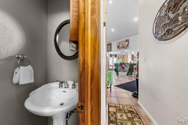 bathroom with baseboards, a textured wall, a sink, and tile patterned floors