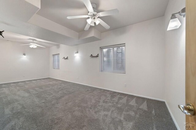 empty room featuring a ceiling fan, dark carpet, and baseboards