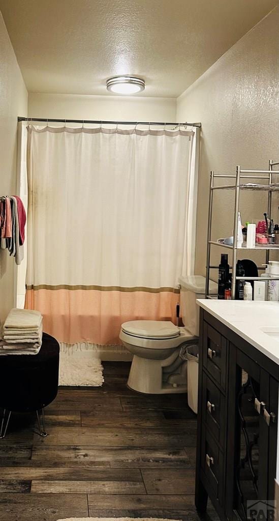 bathroom with a textured ceiling, a textured wall, toilet, wood finished floors, and vanity