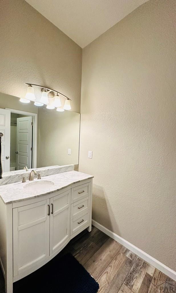 bathroom with a textured wall, vanity, baseboards, and wood finished floors