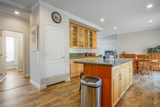 kitchen featuring glass insert cabinets, wood finished floors, dark countertops, a kitchen island, and ornamental molding