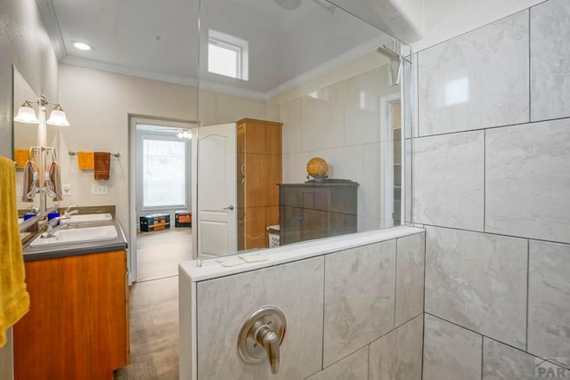 full bath featuring a tile shower, ornamental molding, double vanity, and a sink