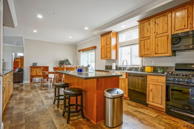kitchen with ornamental molding, black appliances, a breakfast bar area, a kitchen island, and dark countertops