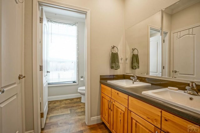 full bath with toilet, double vanity, a sink, and wood finished floors