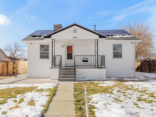 bungalow-style home featuring roof mounted solar panels, fence, a chimney, and stucco siding